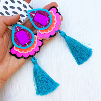 A pair of luxury colourful tassel earrings in bright turquoise, neon pink and purple held in the palm of an open hand