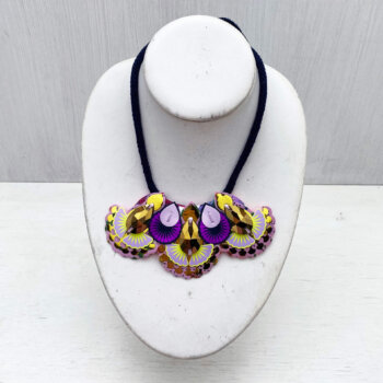 A mini bib necklace in shiny gold and lilac is displayed on a white mannequin neck in front of an off white background