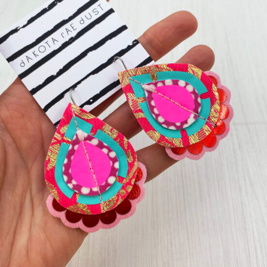 A pair of pink red turquoise recycled fabric earrings held in a open hand