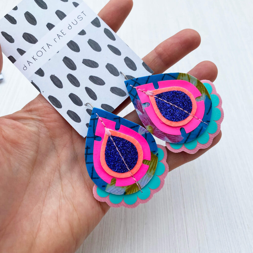 A pair of fluoro pink and blue recycled floral fabric earrings held in a open hand