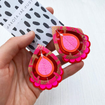 A pair of red pink recycled fabric earrings held in a open hand