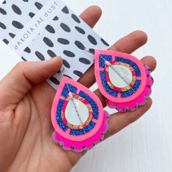 A pair of colourful pink teardrop earrings held in a open hand