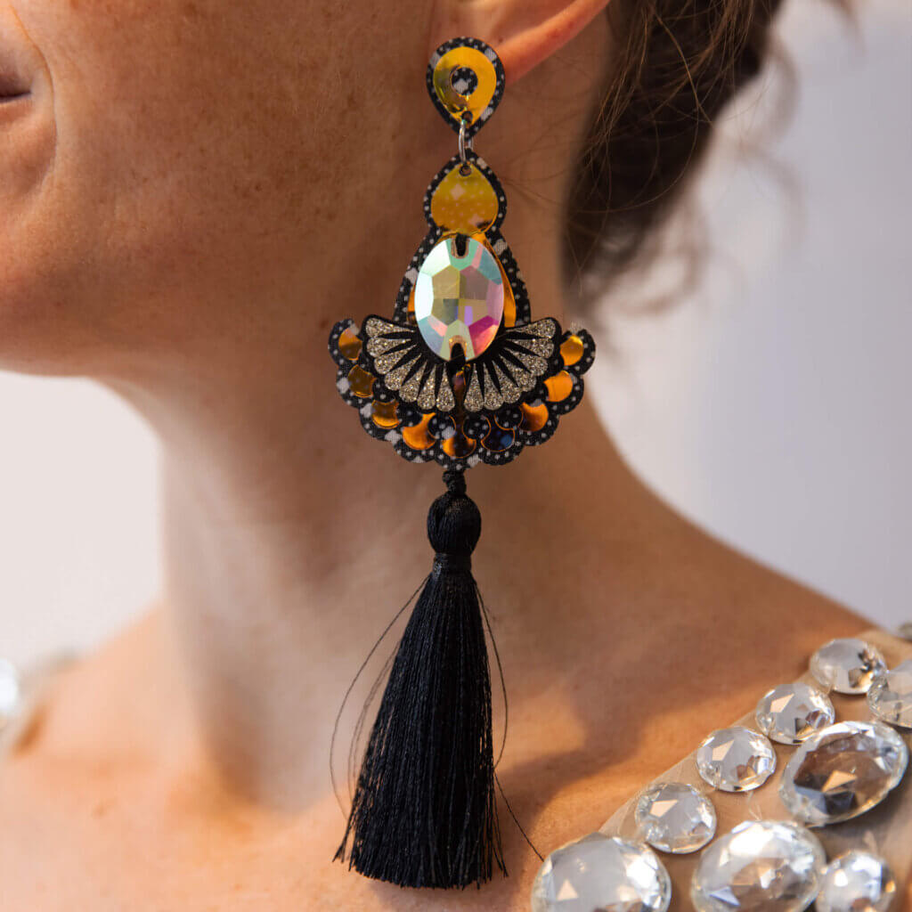A close up of a woman's neck and jawline. She is wearing a pair of dark iridescent tassel earrings.