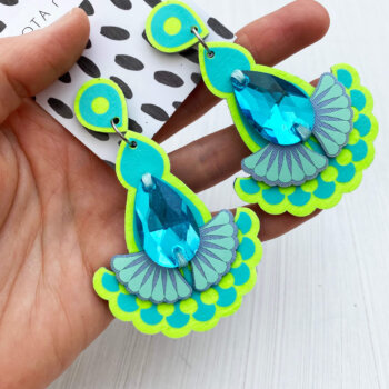 A pair of lime and turquoise jewel earrings are held in an open hand