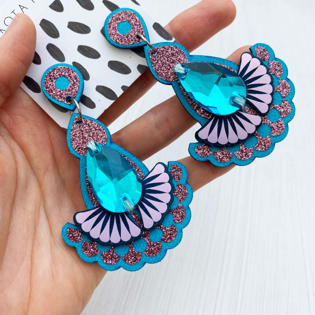 A pair of glittery pink and turquoise jewel earrings are held in an open hand