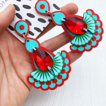 A pair of red and turquoise jewel earrings are held in an open hand