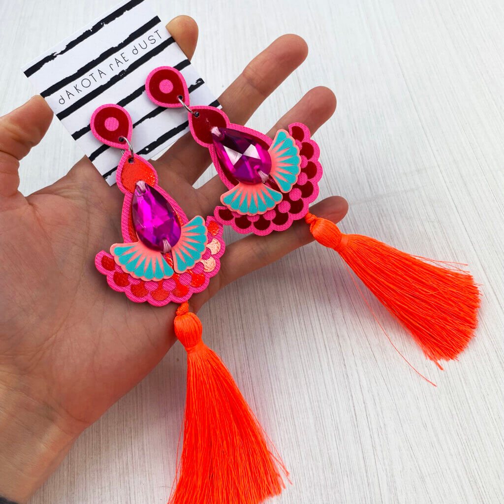 A close up of a pair of jewelled tassel earrings in metallic red, pink and fluorescent orange.