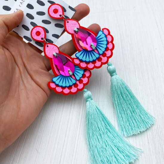 A pair of luxury statement tassel earrings in red, glittery pink and mint are held in an open hand