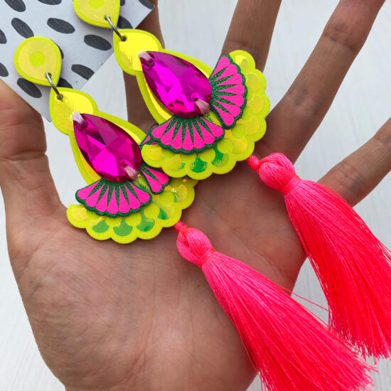 A pair of luxury neon tassel earrings in fluorescent pink and yellow are held in an open hand