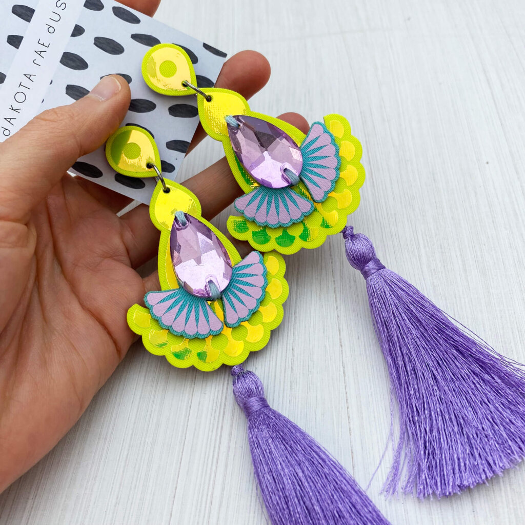 A pair of luxury yellow and lilac tassel earrings are held in an open hand