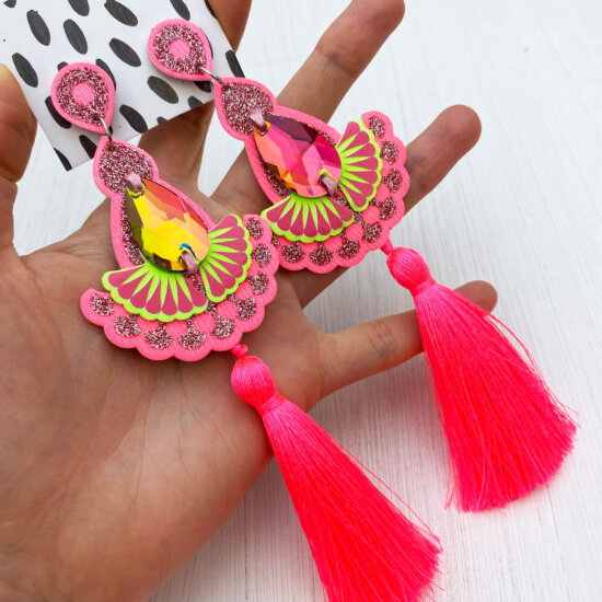 A pair of luxury neon pink and lime green glittery tassel earrings with silky fluoro tassels are held in an open hand