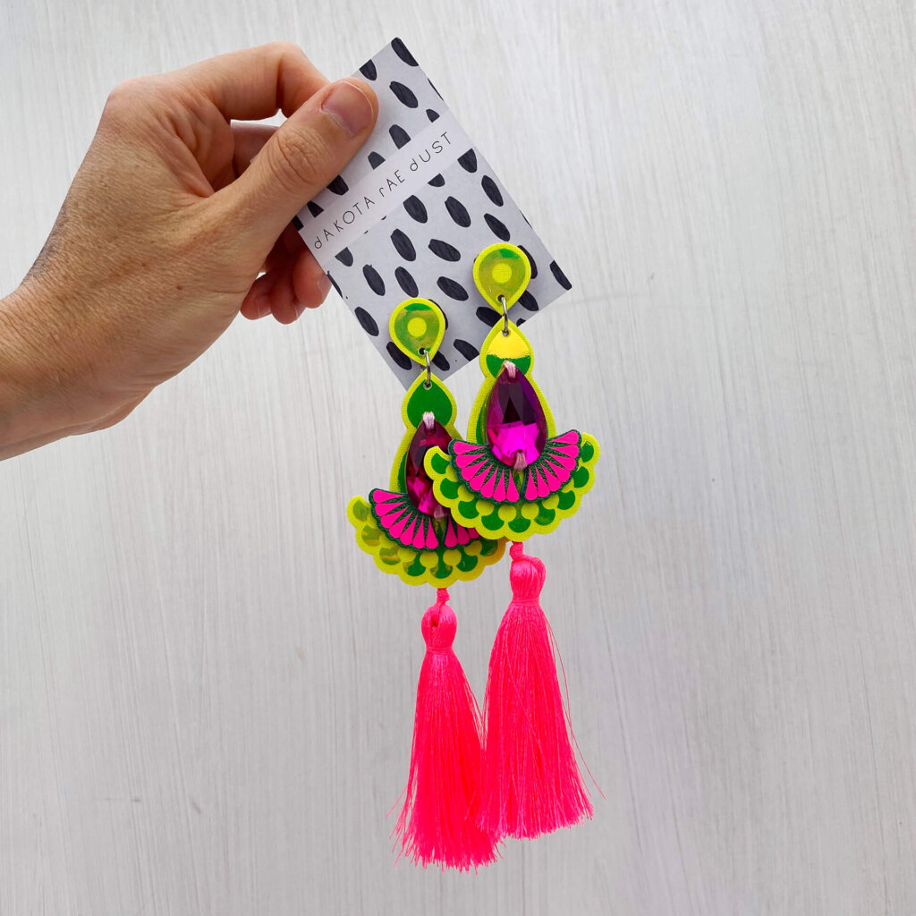 A pair of luxury neon tassel earrings in fluorescent pink and yellow are held in an open hand