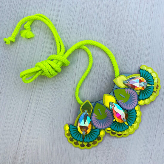 An iridescent and fluorescent yellow mini bib necklace with light blue cords on an off white background