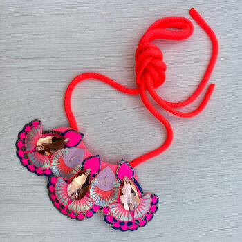A blue, coral and neon pink mini bib necklace with light blue cords on an off white background