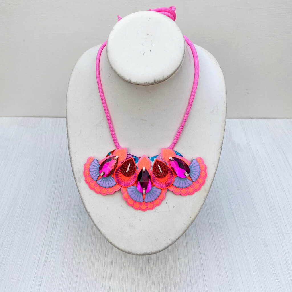A lilac, orange and pink mini bib necklace with pink cords is displayed on a white mannequin neck
