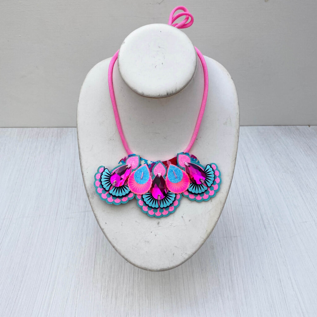 A blue and pink mini statement necklace with pink cords is displayed on a mannequin neck