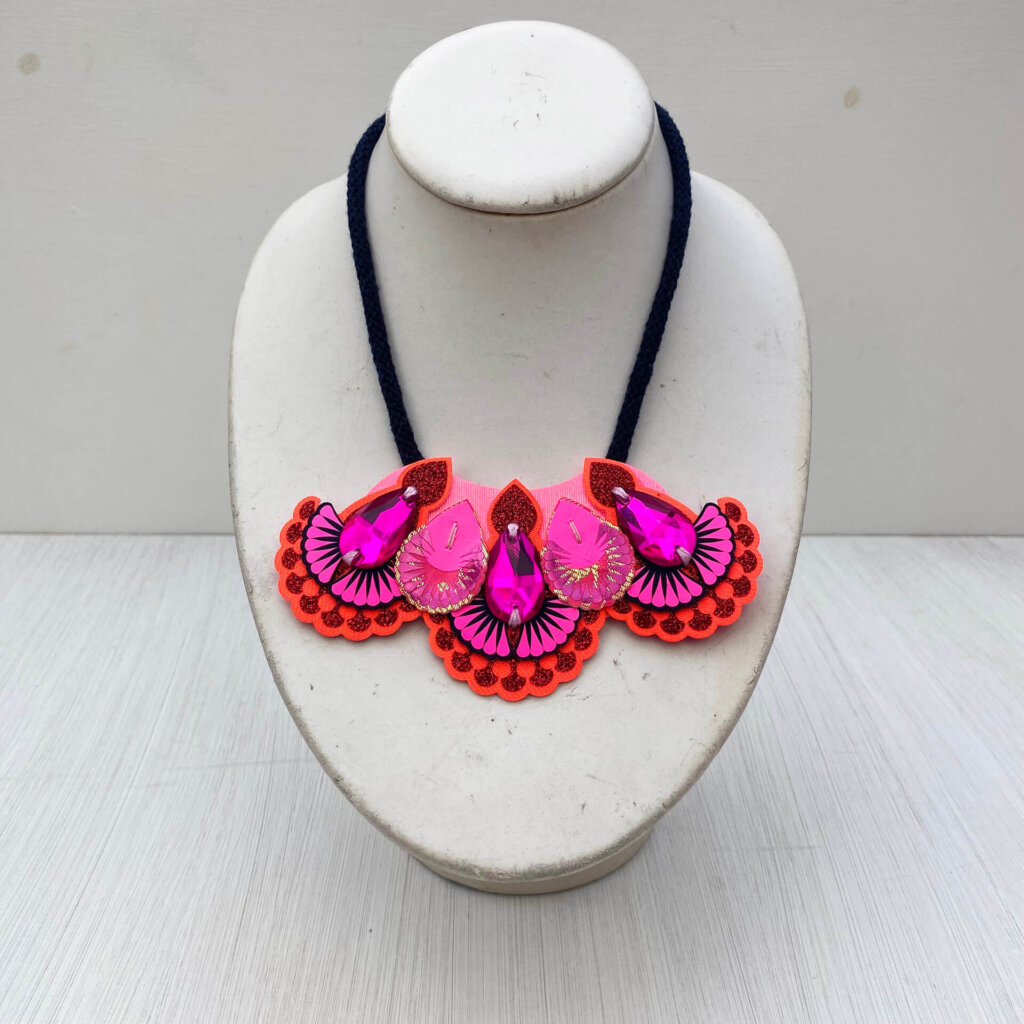 A navy, orange and hot pink mini bib necklace with navy cords is displayed on a white mannequin neck