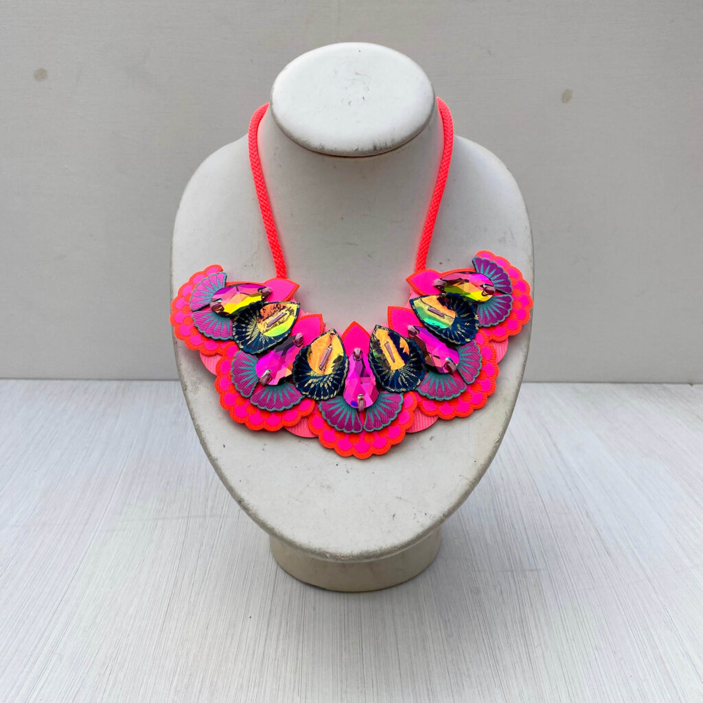 A neon pink, orange and navy oversize statement bib necklace with neon coral cord ties and dark iridescent jewels displayed an off white mannequin neck