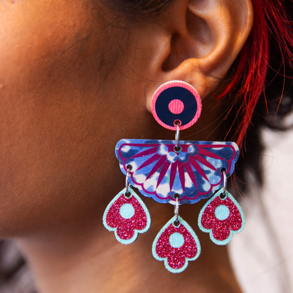 A close up of a woman's ear and neck, focused on the chandelier style, jangly droplet earrings she is wearing.