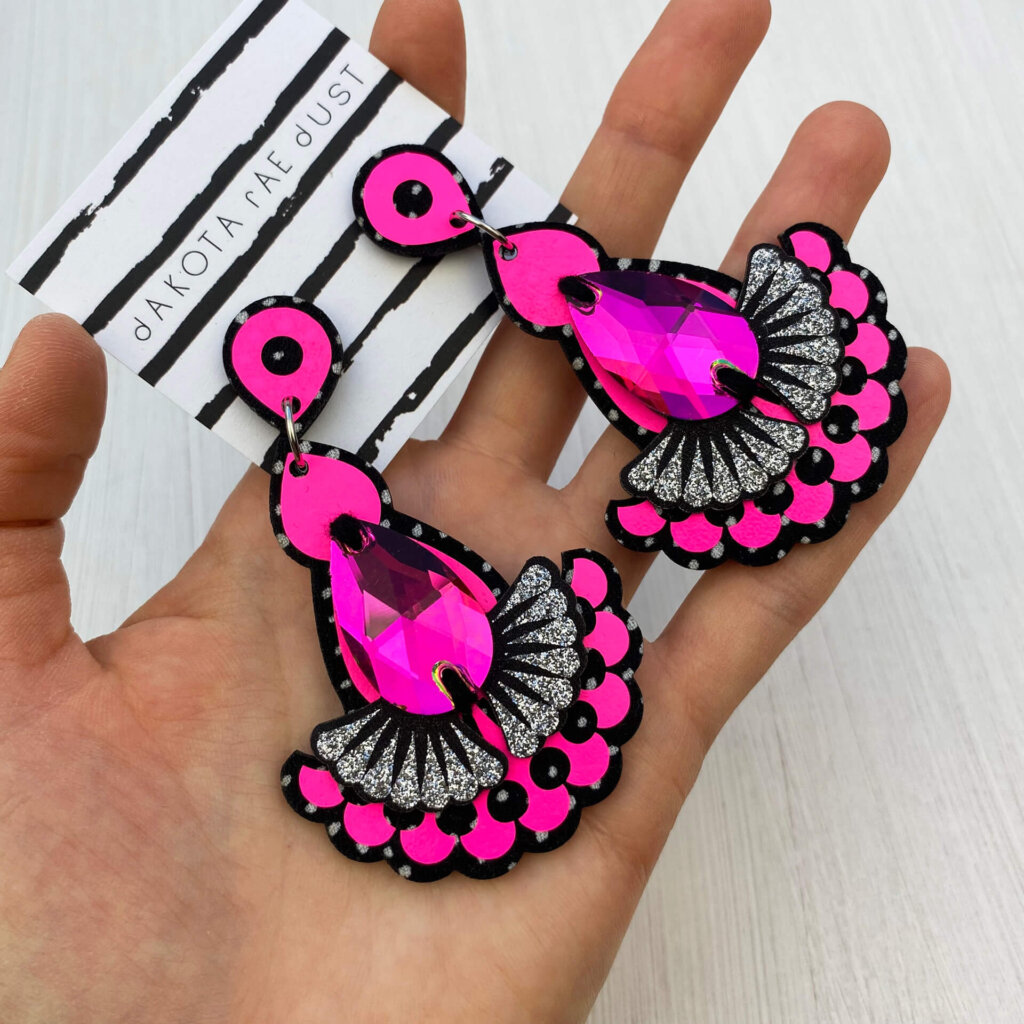 A pair of neon pink jewel earrings are held in an open hand