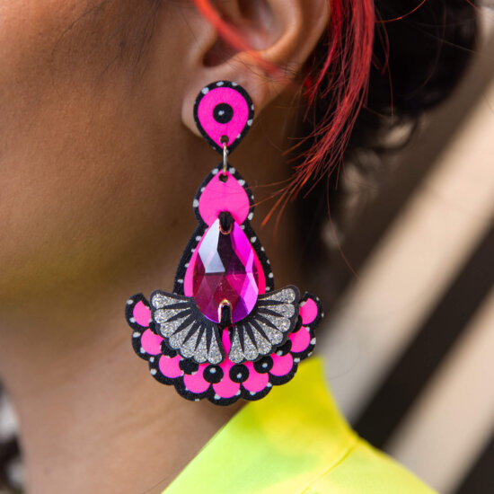 A close up of a woman's ear and jawline focusing on her neon pink jewel earrings.