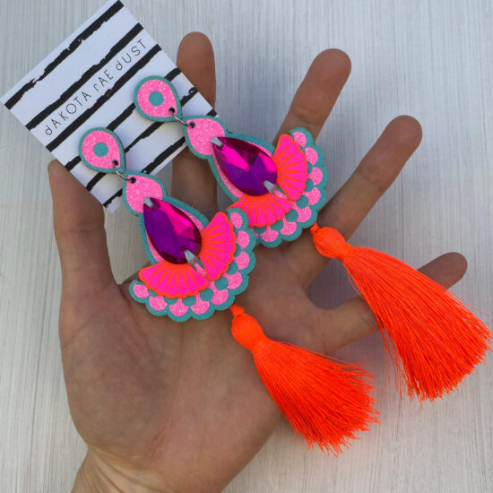 A pair of fluorescent orange, glittery pink and blue colour popping tassel earrings are held in an open hand