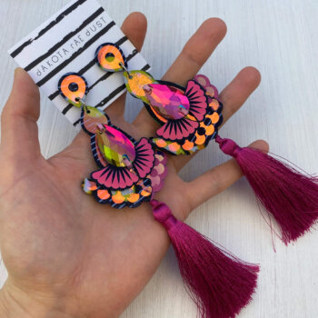 A pair of dark pink iridescent tassel earrings are held in an open hand