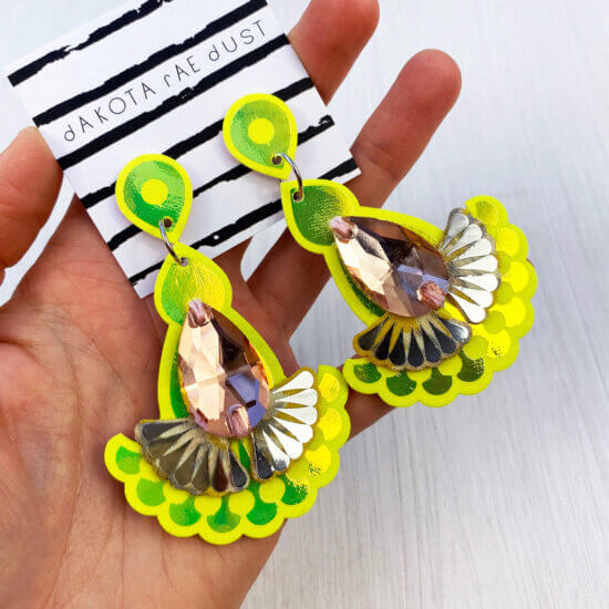 A pair of iridescent, peach and yellow jewel earrings are held in an open hand