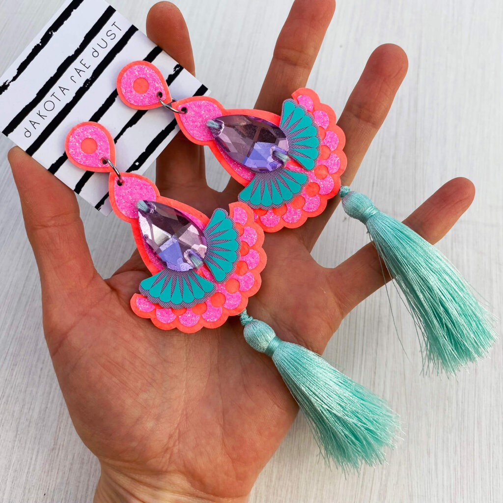 A pair of pastel silky tassel earrings in coral mint and lilac are held in an open hand