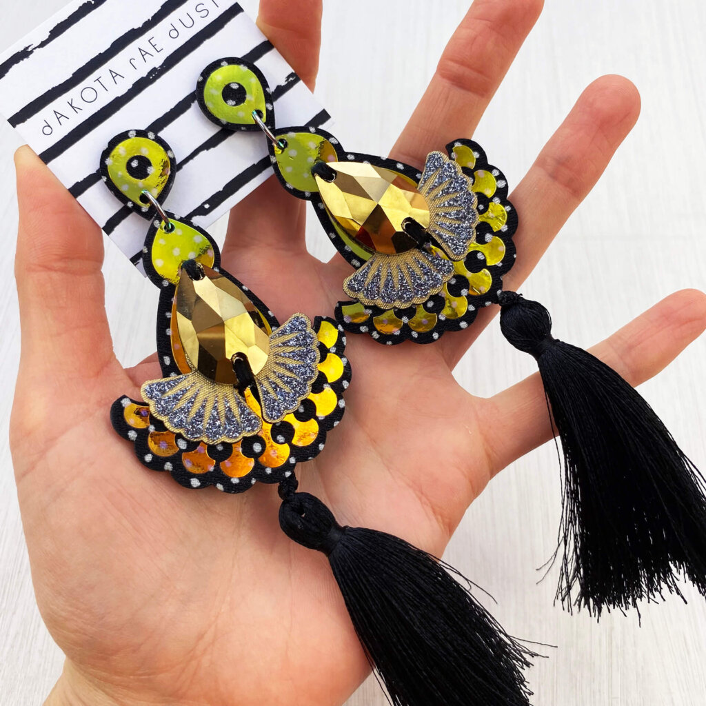 A pair of black gold tassel earrings are held in an open hand