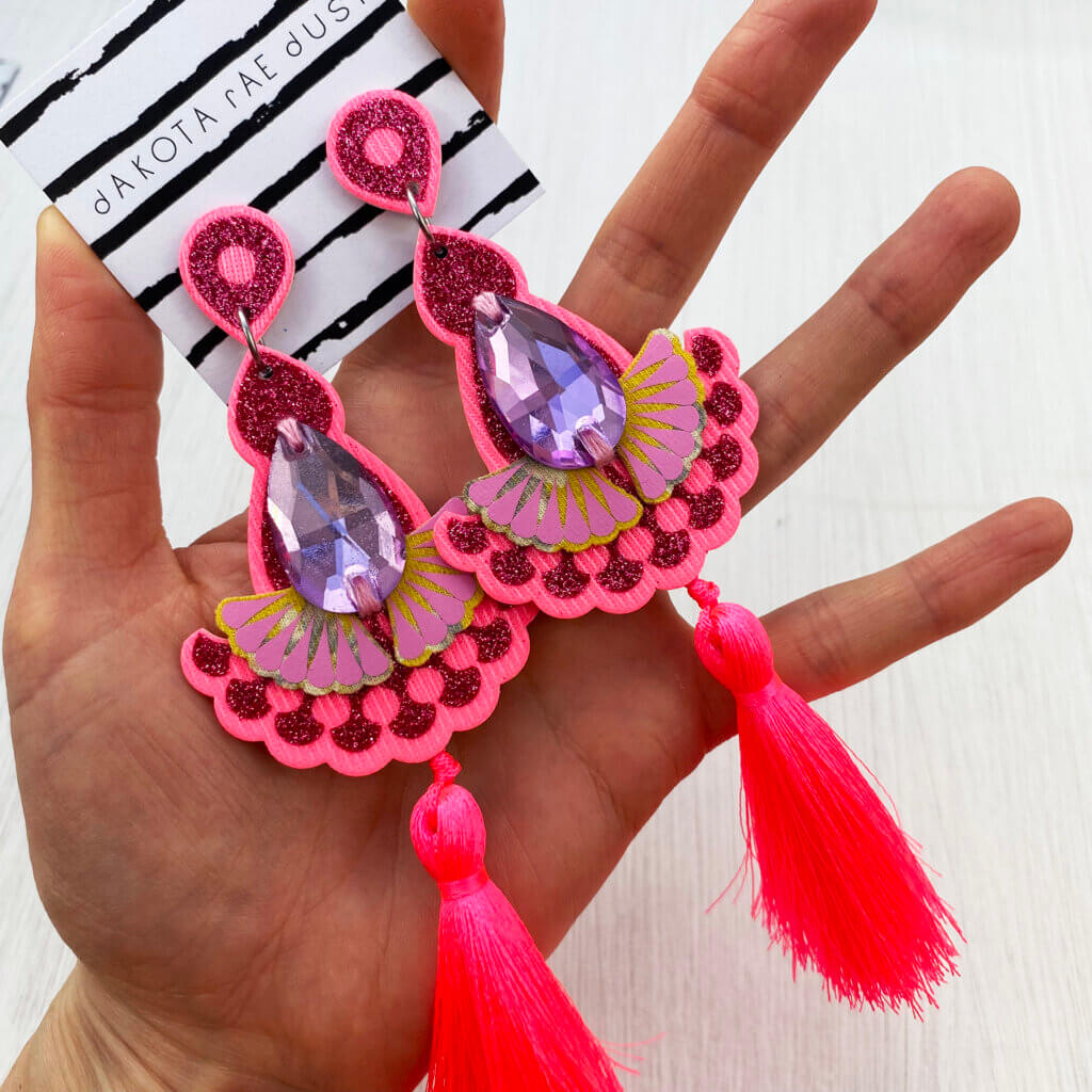 A pair of glittery pink tassel earrings are held in an open hand
