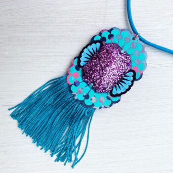 A custom cast giant jewel pendant necklace with a turquoise blue fringe lying on an off white background