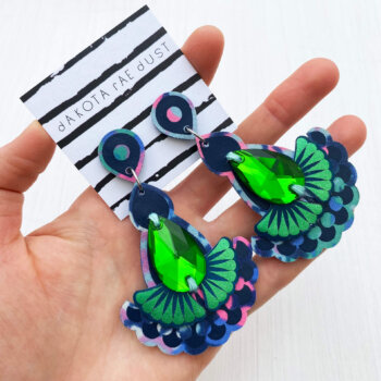 A pair of navy blue and green jewel earrings are held in an open hand