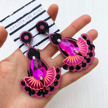 A pair of glittery black and pink jewel earrings are held in an open hand
