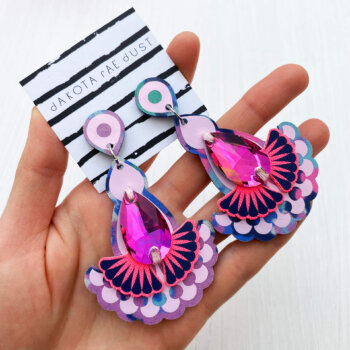 A pair of floral fabric pink jewel earrings are held in an open hand