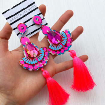A pair of pink floral luxury tassel earrings are held in an open hand
