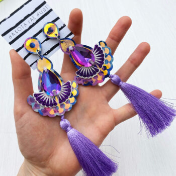 A pair of lilac luxury tassel earrings are held in an open hand