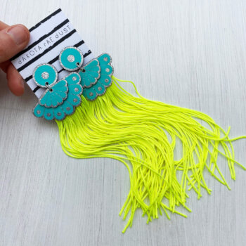 A pair of fan and fluoro fringe earrings are held in an open hand