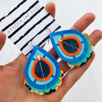 A pair of turquoise orange fabric earrings held in a open hand