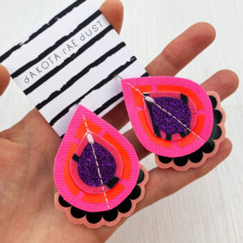 A pair of purple black pink red fabric earrings held in a open hand