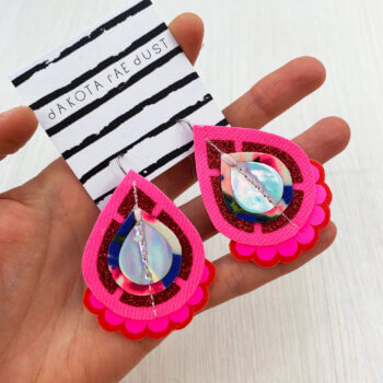 A pair of pink red glitter fabric earrings held in a open hand