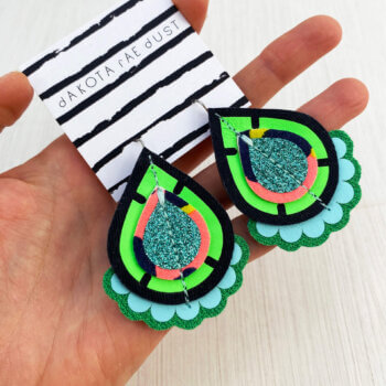 A pair of bright green teardrop earrings held in a open hand