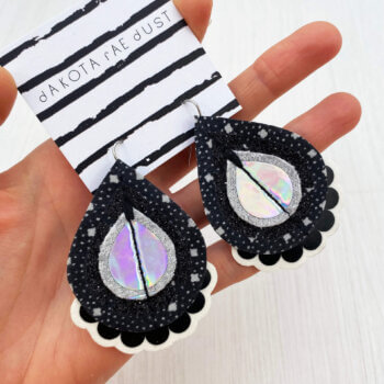 A pair of monochrome patterned fabric earrings held in a open hand