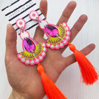 A pair of neon tassel earrings are held in an open hand